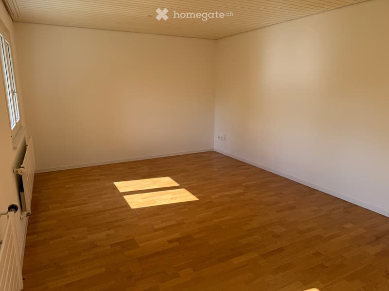 Empty room with wooden flooring and white walls, featuring a window and radiator on one side.