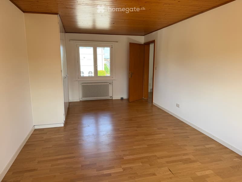 Empty room with wooden flooring, white walls, a window with a radiator below, and a wooden door leading to another space.