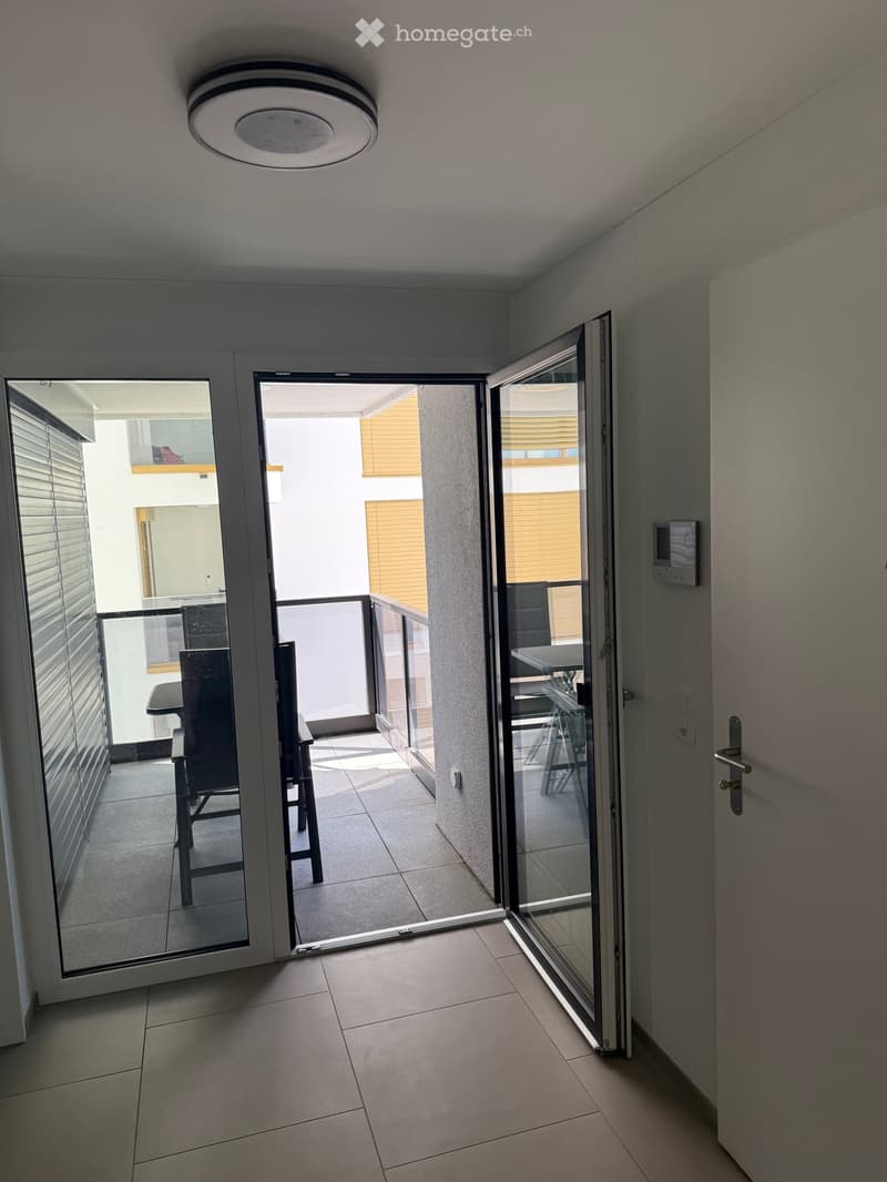 Hallway with tiled floor, large sliding glass doors leading to a balcony with a table and chairs.