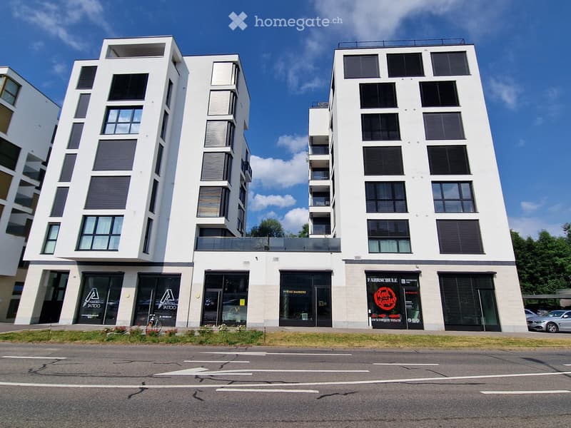 Modern multi-story building with white facade, large windows, and commercial storefronts at ground level.
