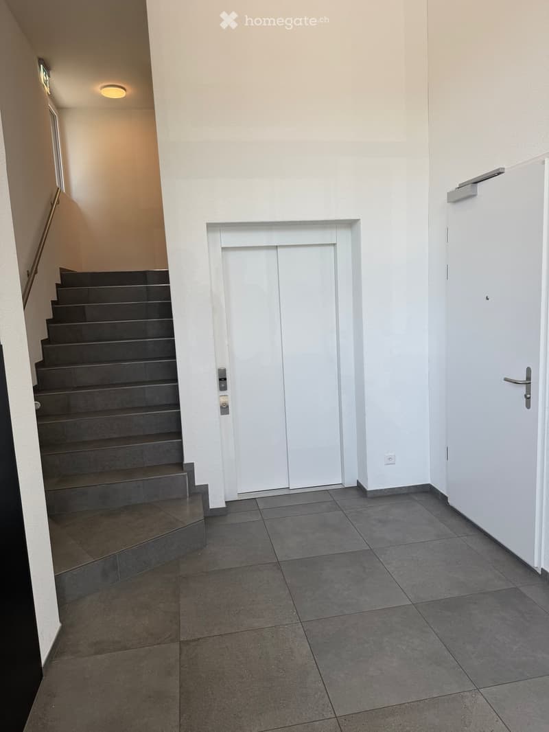 Empty hallway with tiled floor, white walls, staircase leading upwards, and a closed white door.