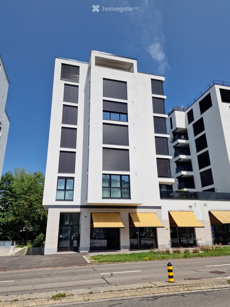 Modern multi-story building with white facade, large windows, and yellow awnings over ground-floor storefronts.