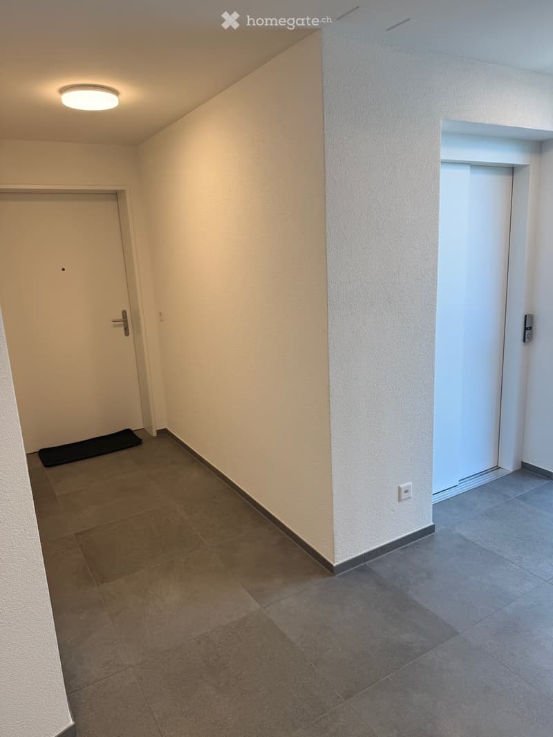 Empty hallway with tiled floor, white walls, two doors, and a small black mat near one door.