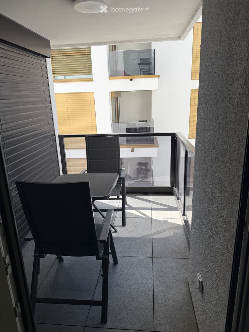 Balcony with a table and chairs, modern glass railing, and view of the interior space.