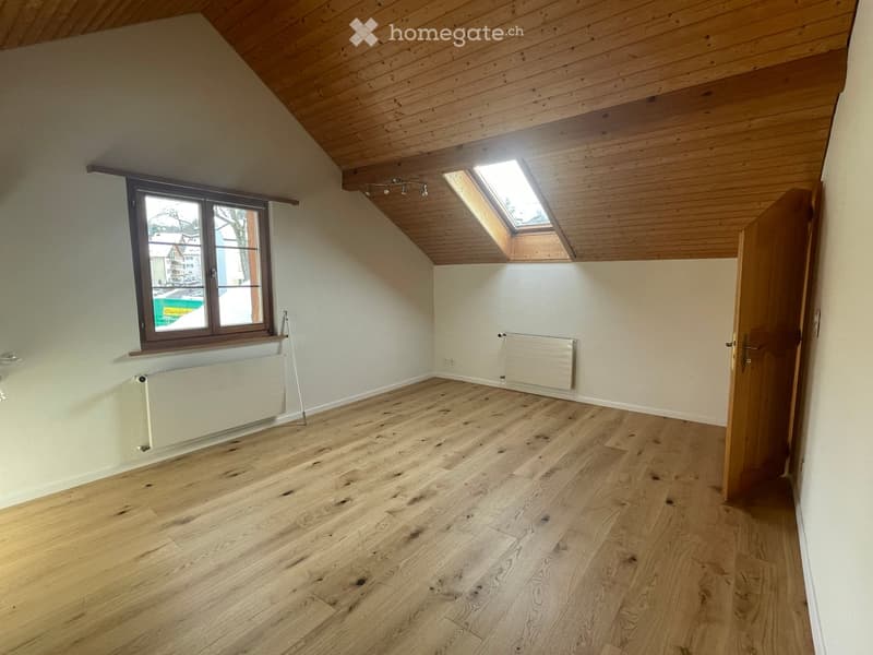 Empty room with wooden flooring, white walls, a skylight window, and a door leading to another space.