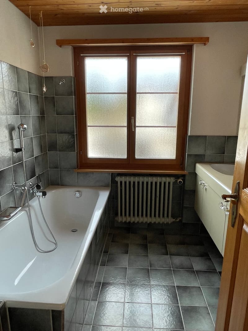 Bathroom with a bathtub, sink, radiator, and window with frosted glass panels.