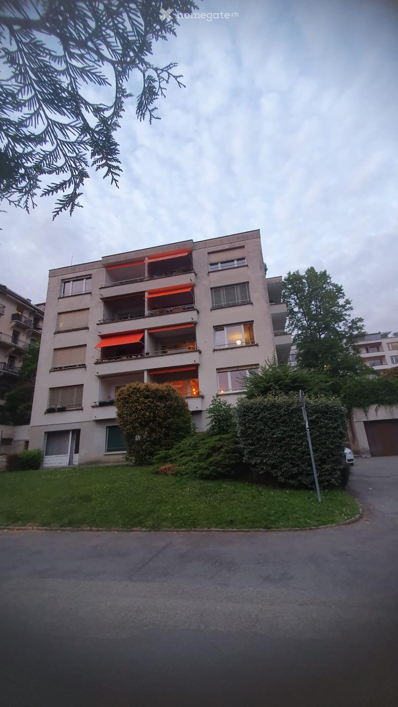 Multi-story residential building with balconies, orange awnings, and surrounding greenery.