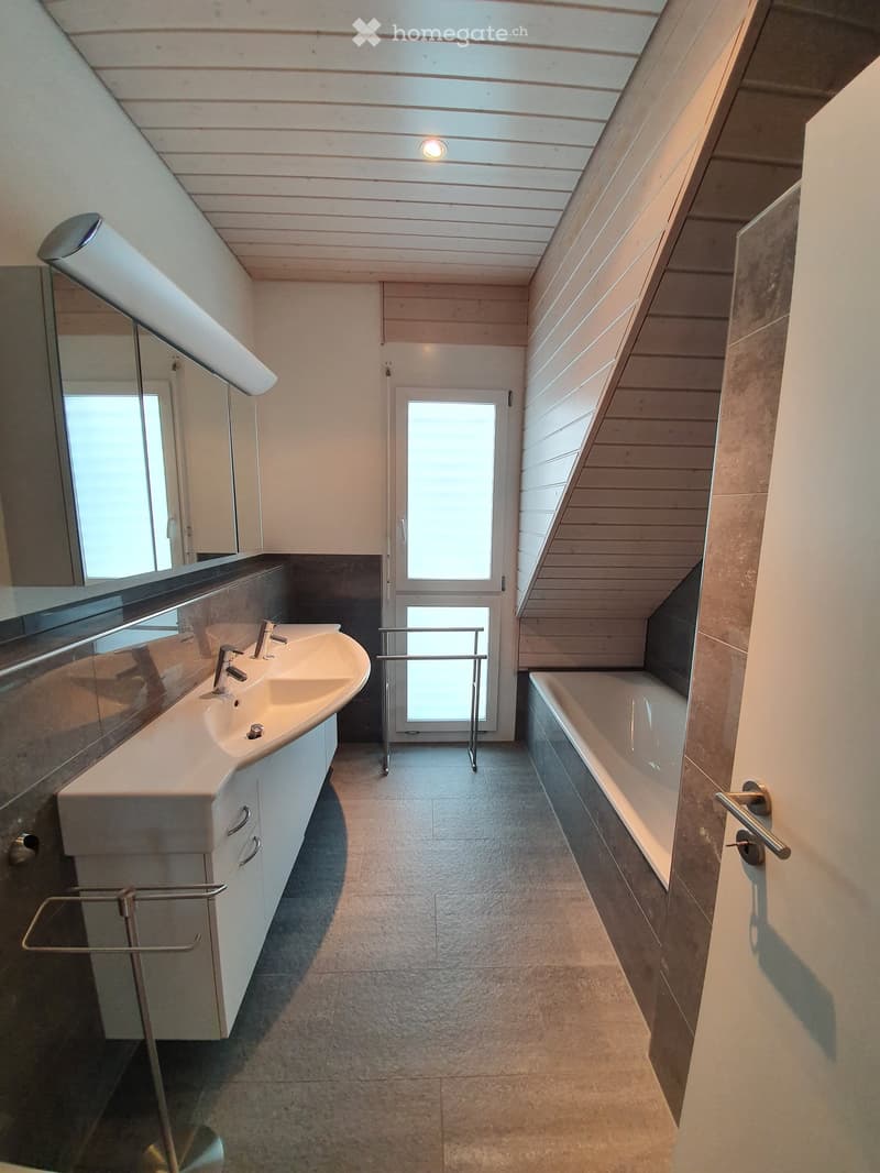 Modern bathroom with a double sink, bathtub, large mirror, and a glass door leading to a balcony.