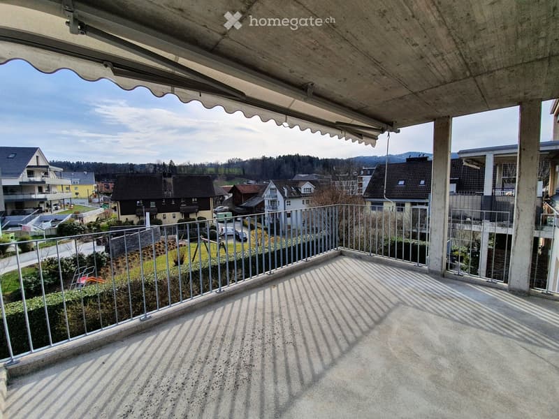 Balcony with metal railing, concrete floor, and a view of a residential neighborhood with houses and greenery.