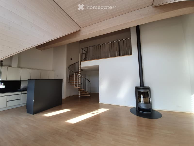 Open-plan living space with light wooden flooring, modern kitchen cabinets, a spiral staircase leading to an upper level, and a contemporary wood-burning fireplace.