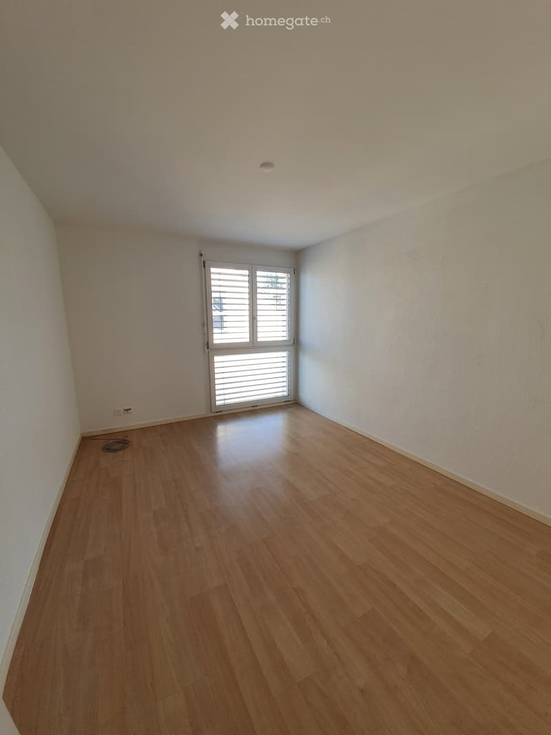 Empty room with light wooden flooring, white walls, and a large window with blinds. No furniture or equipment is present.