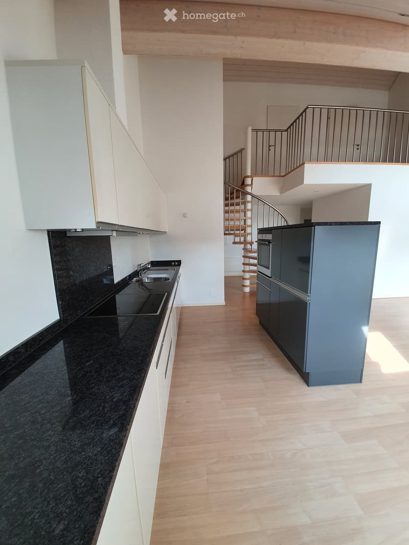 Modern kitchen with white cabinets, black granite countertops, stainless steel appliances, and a spiral staircase leading to an upper level.