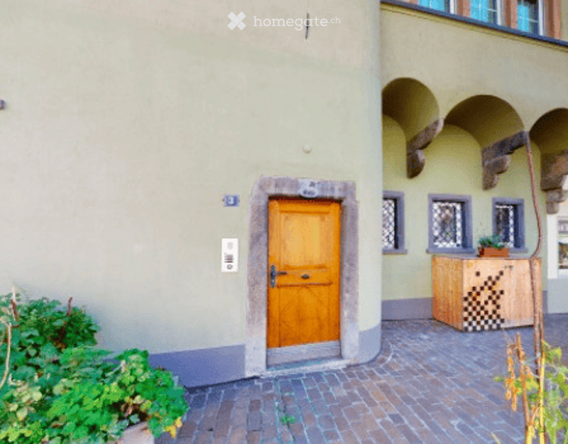 Facade of a building with a wooden door, small potted plant, and a checkered wooden bench.