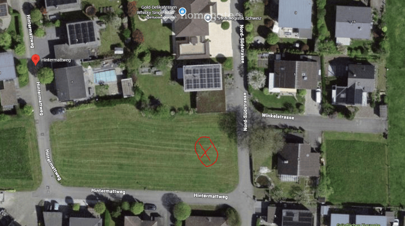 Aerial view of a residential area with multiple houses, green spaces, and a swimming pool visible in the neighborhood.