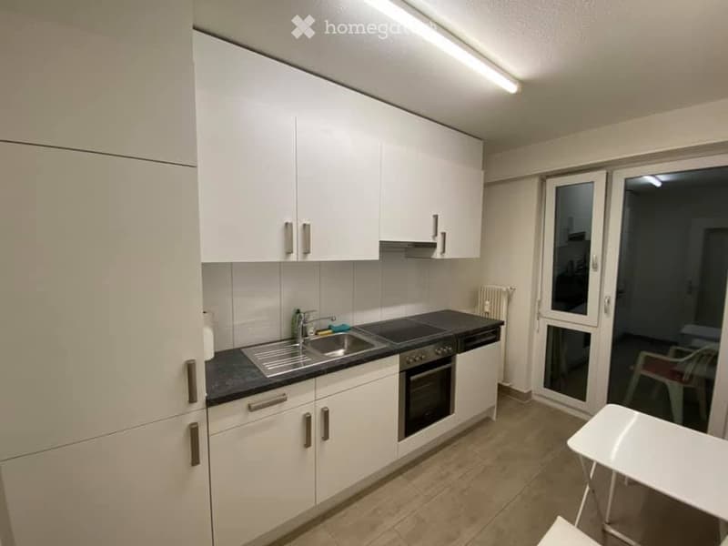 Modern kitchen with white cabinets, stainless steel sink, oven, dishwasher, and a small table near the window.