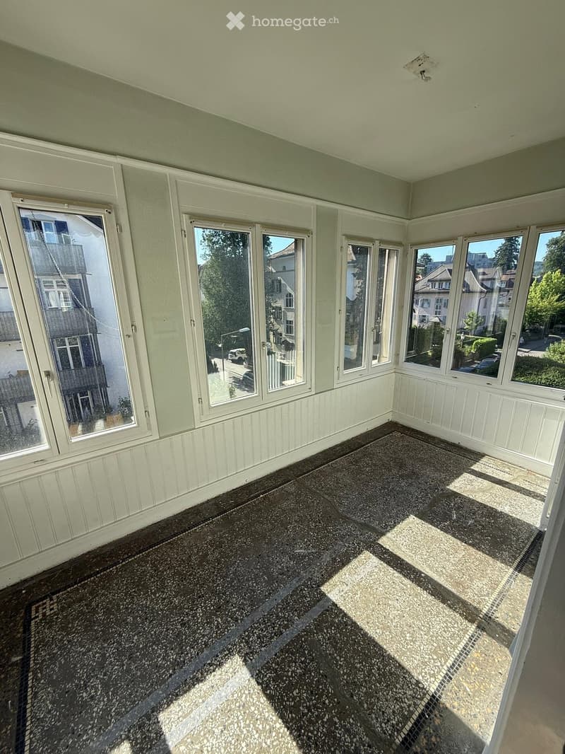 Empty sunroom with large windows, light green walls, and a dark speckled floor.