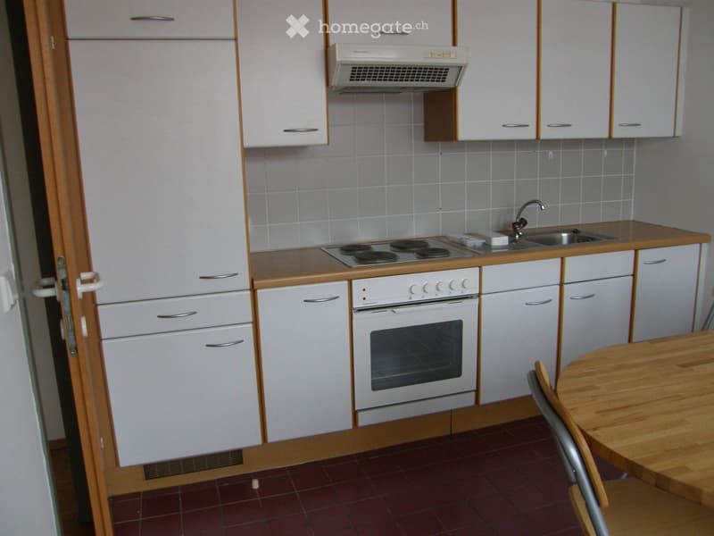 Compact kitchen with white cabinets, a stove, an oven, a sink, and a small dining area with a table and chair.