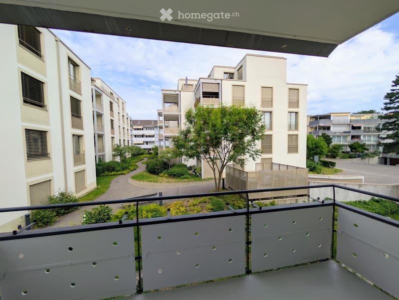 Balcony overlooking a modern residential complex with multiple buildings, greenery, and pathways.