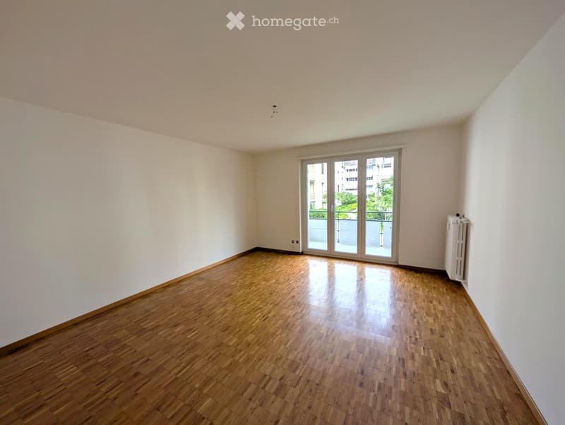Empty room with wooden flooring, white walls, and a large sliding glass door leading to a balcony.
