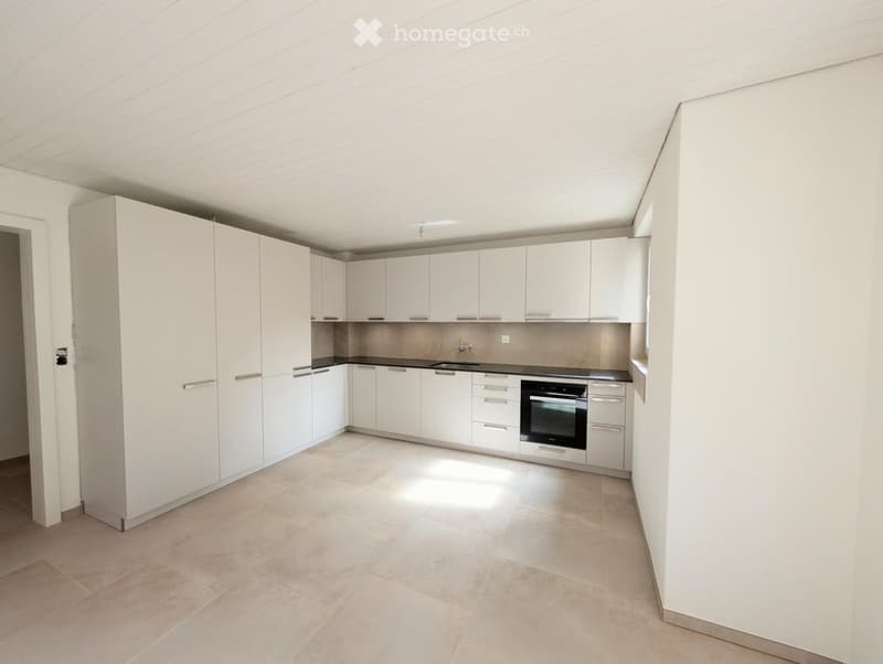 Modern kitchen with white cabinets, a black countertop, and a built-in oven. The floor is tiled in a light beige color.