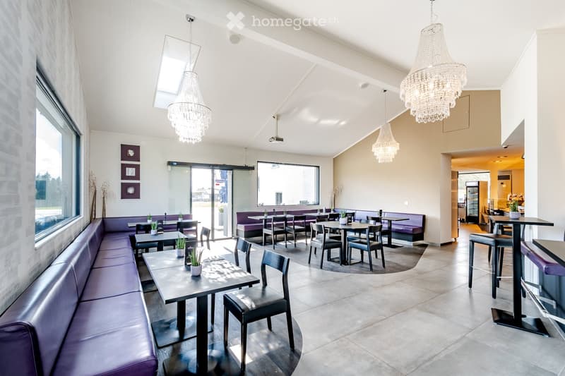 Modern restaurant interior with seating areas, tables, chairs, and chandeliers.