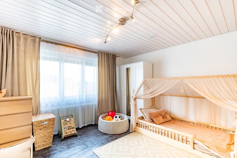 Cozy children's bedroom with a wooden bed, canopy, wicker basket, toy cart, and various toys.