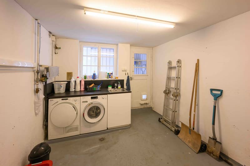 Utility room with washing machine, dishwasher, sink, cleaning supplies, ladder, and shovel.