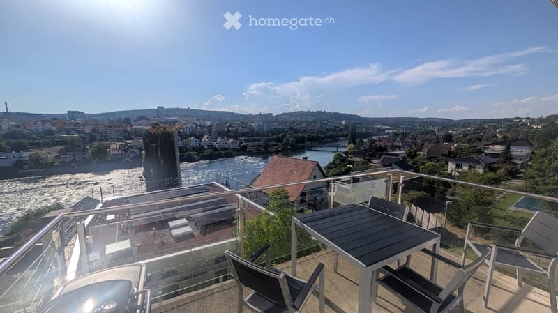 Balcony with a view of a river and cityscape, featuring a table and chairs.