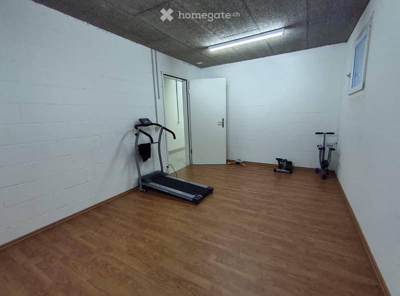 Exercise room with wooden flooring, white brick walls, a treadmill, an exercise bike, and a door leading to another room.