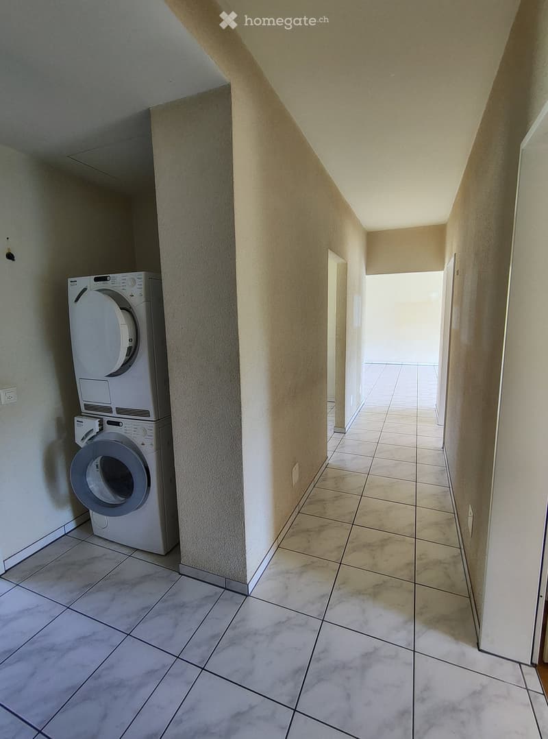 Hallway with tiled flooring, beige walls, and a private washing machine on the left side.