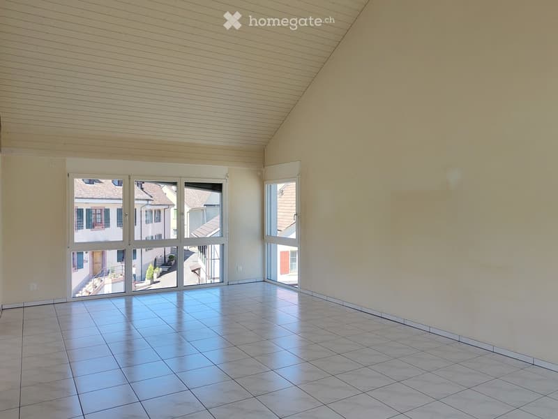 Empty room with tiled floor, large windows, and wooden ceiling beams.