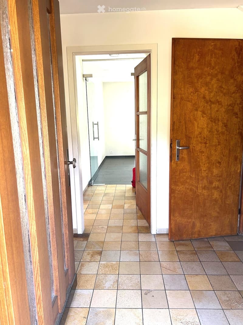 Empty hallway with tiled floor, wooden doors, and a visible room at the end.