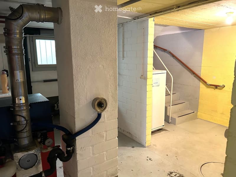 Empty basement space with exposed brick walls, concrete floor, metal staircase, and various utility equipment including a water heater and boiler.