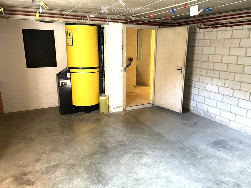 Empty basement or utility room with concrete floor, exposed brick walls, a large yellow water tank, and an open doorway leading to another space.