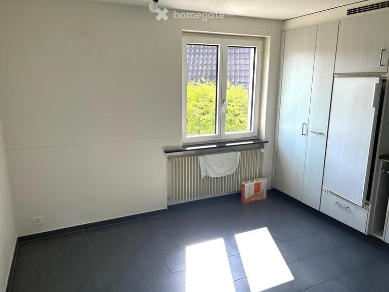 Empty room with dark tiled floor, white walls, a window with a view of greenery, a radiator with a towel, and a stack of paper towels on the floor.