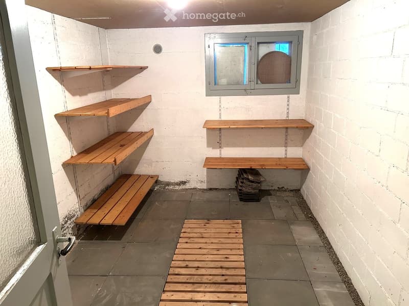 Empty room with white brick walls, concrete floor, wooden shelves, and a small window with a metal frame.