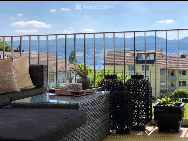 Balcony with a scenic mountain view, featuring a wicker sofa, glass coffee table, potted plants, and decorative lanterns.