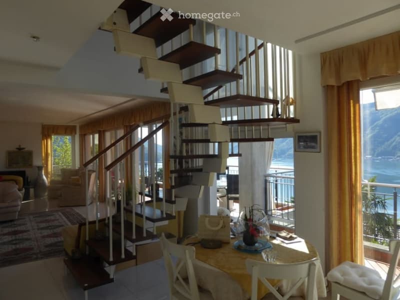 Open-concept living space with wooden staircase, large windows overlooking a balcony and scenic view, dining table, and cozy furnishings