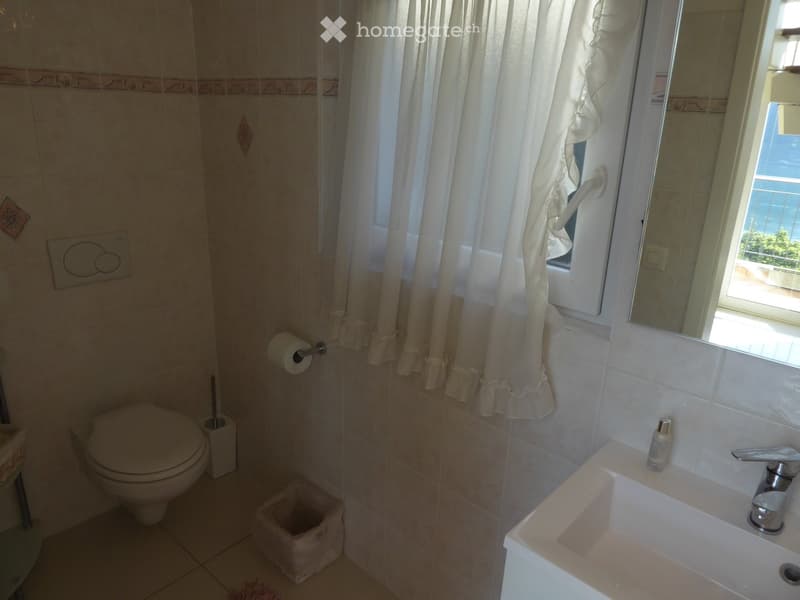 Bathroom with white tile walls, toilet, sink, and curtained window