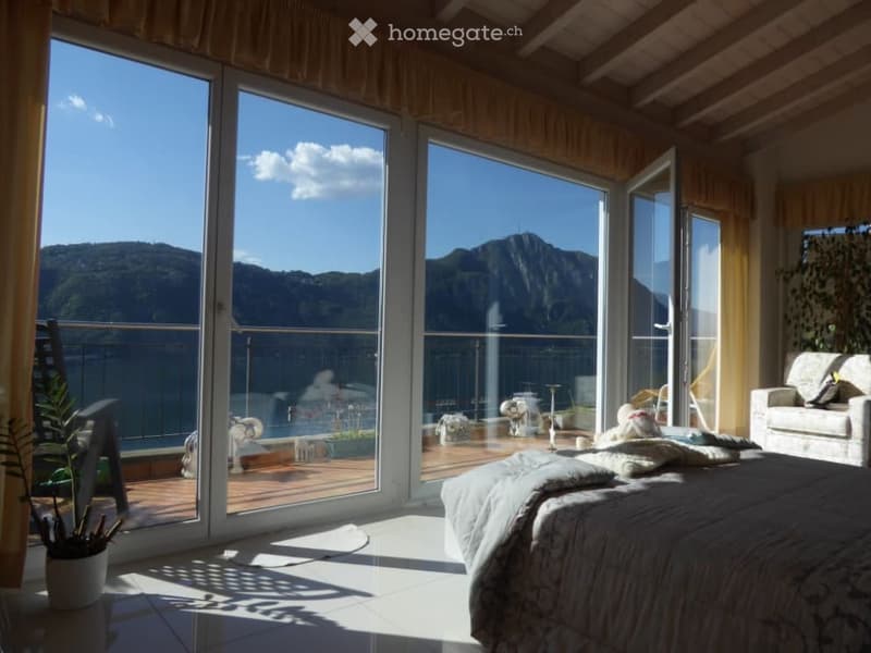 Spacious bedroom with large windows offering a scenic mountain view, wooden ceiling, cozy bedding, and a sofa in the corner.