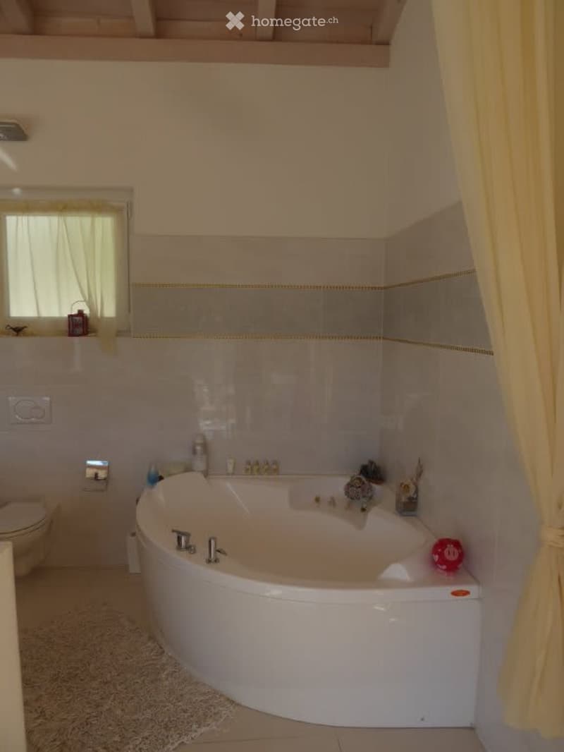 Spacious bathroom with a large corner bathtub, tiled walls, and a window providing natural light