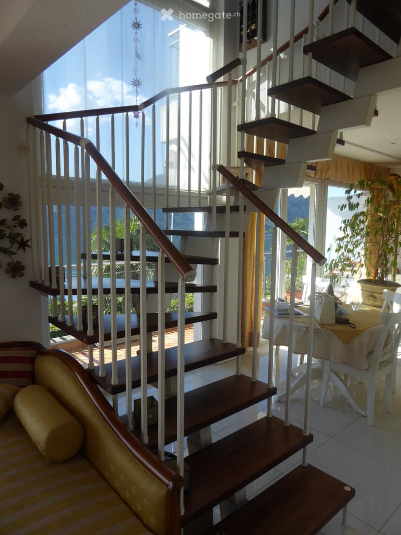 Spiral staircase with wooden steps and metal railings, leading to a balcony or terrace with a view of the outdoors. The space also includes a dining area with a table and chairs.