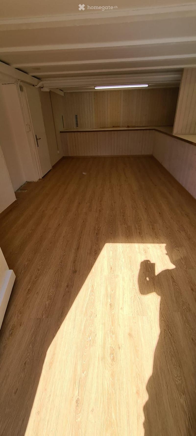 Empty room with wooden flooring and light-colored walls, featuring a closet with wooden doors and a small shelf.