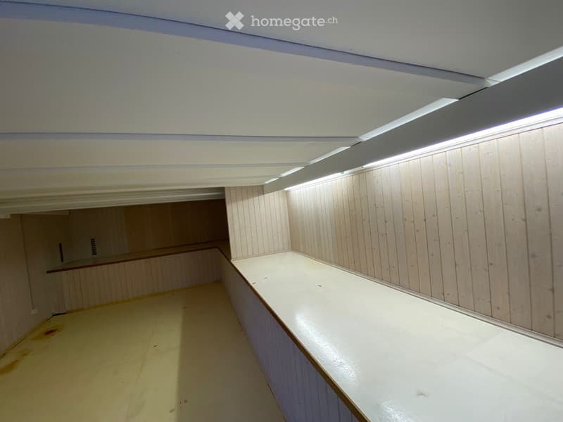 Empty room with wooden panel walls and a white countertop, illuminated by LED strip lighting.