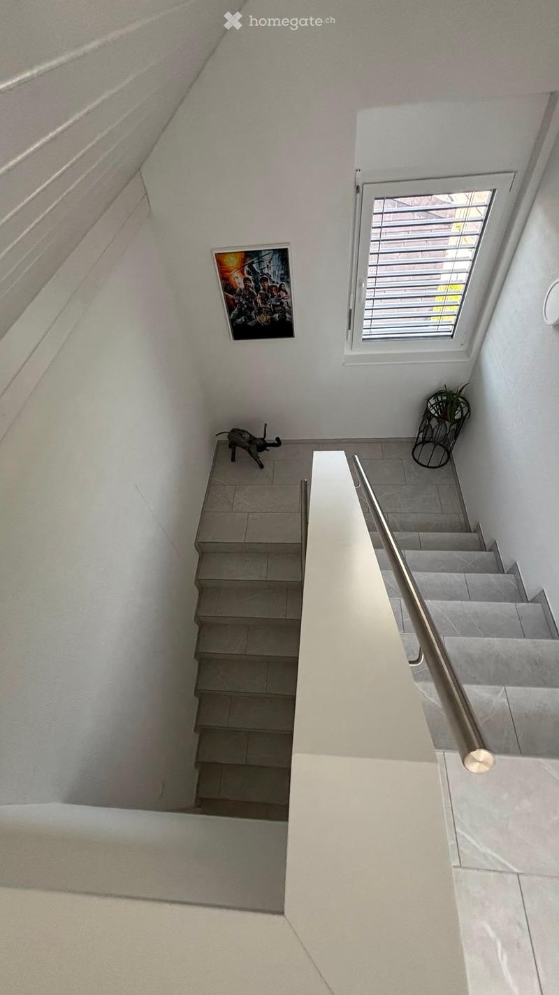 Modern staircase with grey tiled steps, white walls, a metal handrail, a small window, a framed picture, and a small decorative plant in a black pot.