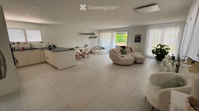 Open-plan living and dining area with a modern kitchen island, a sofa, a chair, a dining table, and a laptop on the island.