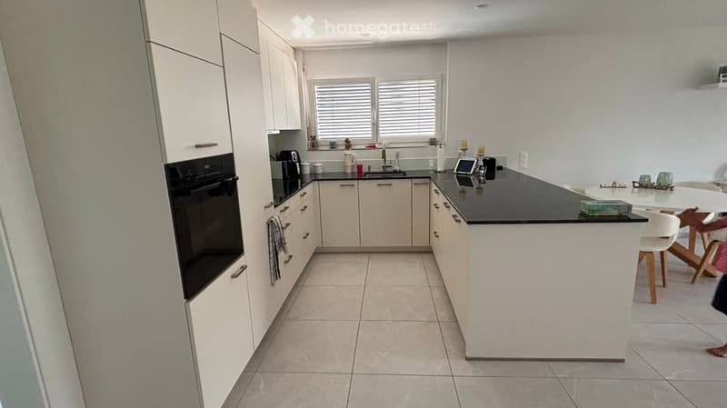 Modern kitchen with white cabinets, black countertop, built-in oven, sink, and small dining area with a table and chairs.