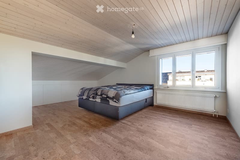 Modern bedroom with wooden slatted ceiling, large windows, and a bed with a blue and grey duvet.