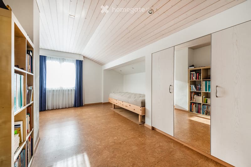 Modern bedroom with wooden floor, slanted wooden ceiling, built-in bed, large bookshelf, and wardrobe.