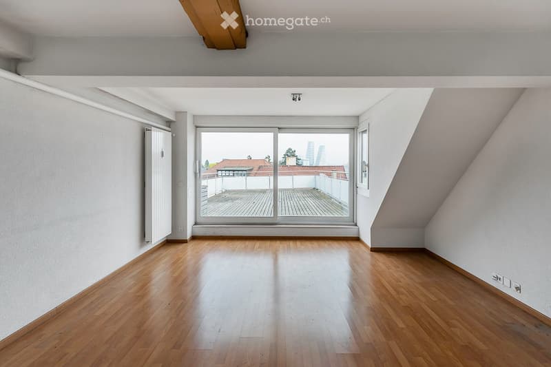 Empty room with wooden flooring, white walls, large window with a view of a rooftop terrace, and a radiator on the left side.